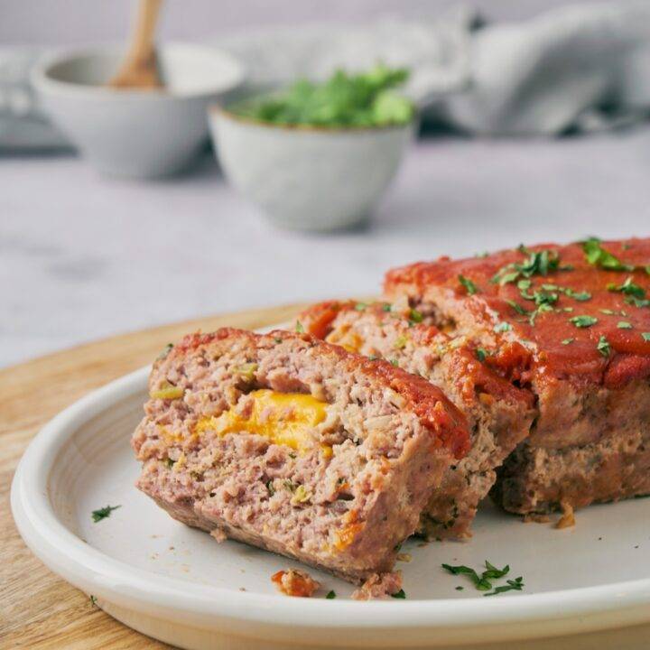 Meatloaf covered in red sauce with two slices cut and laid on top of each other. The meatloaf is filled with melted cheese.