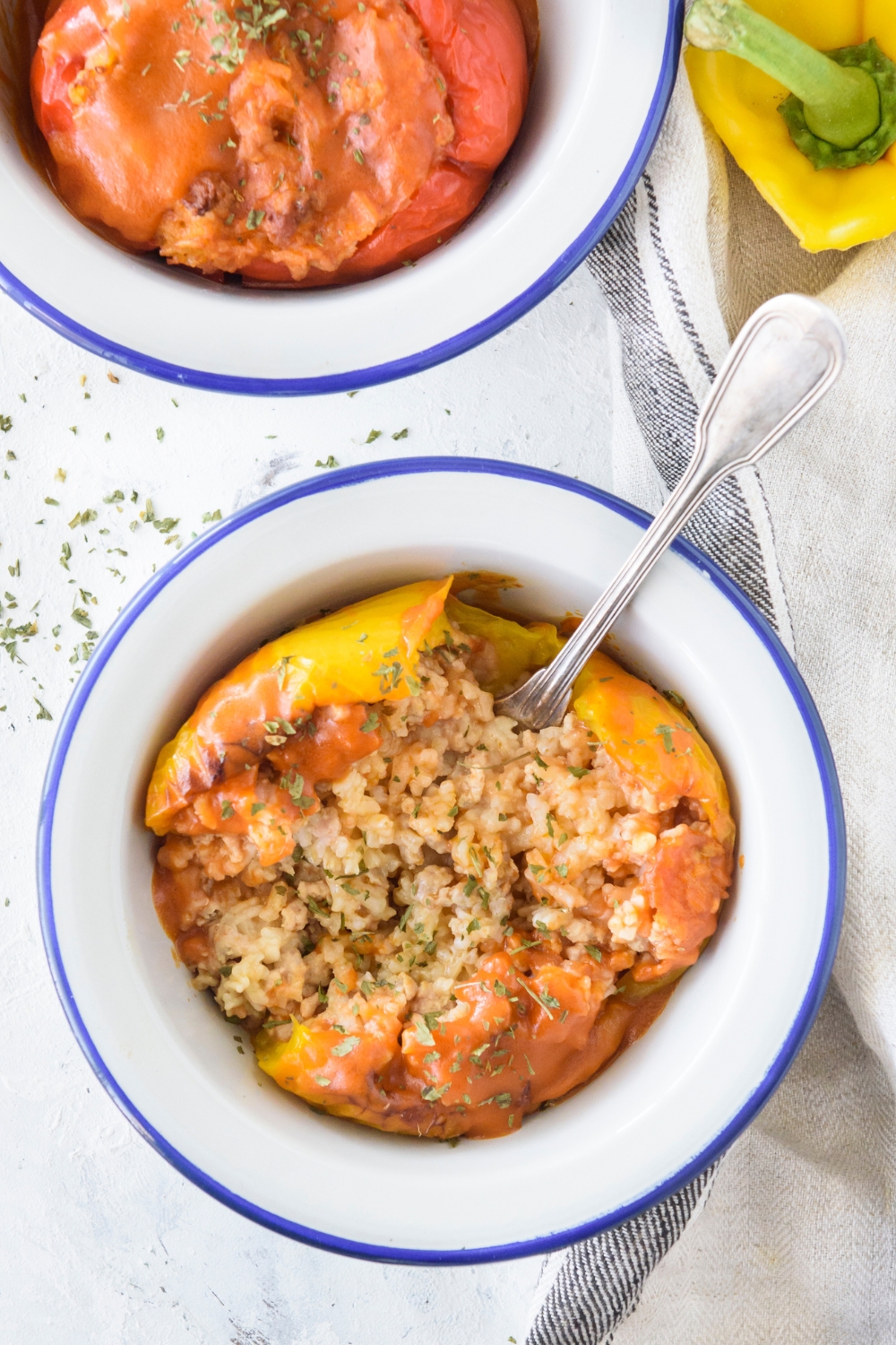 A bowl with a yellow bell pepper stuffed with rice and ground meat and topped with seasonings.