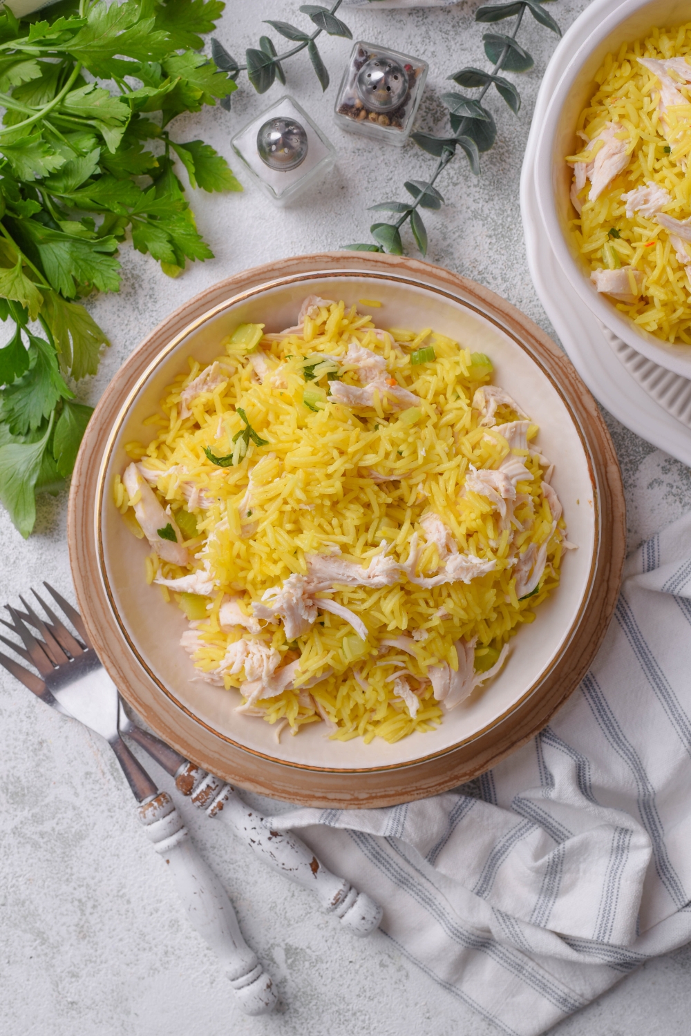 Overhead view of a bowl of yellow rice and shredded chicken mixed together. A second bowl of chicken and rice is next to it along with two forks.