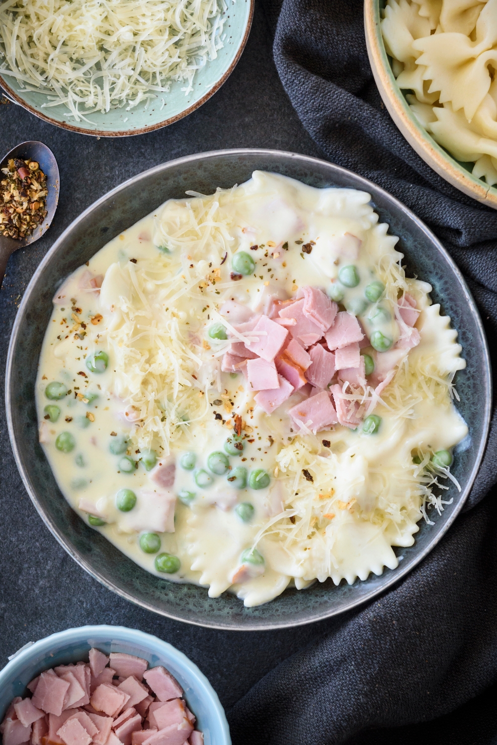 A bowl filled with pasta, ham, peas, and shredded cheese covered in cream sauce.