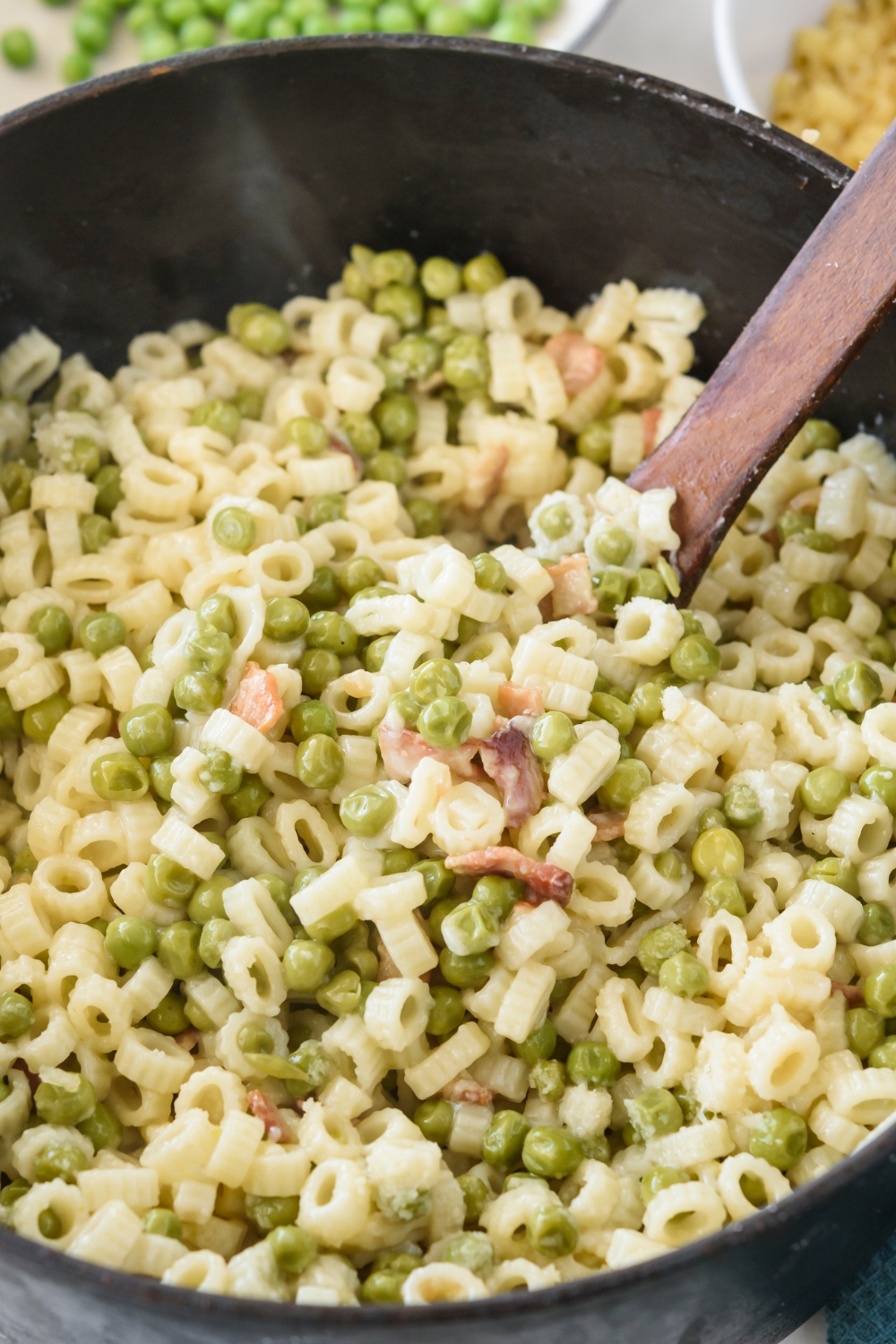 Pasta with peas mixed in a pot with a wooden spoon submerged in it.