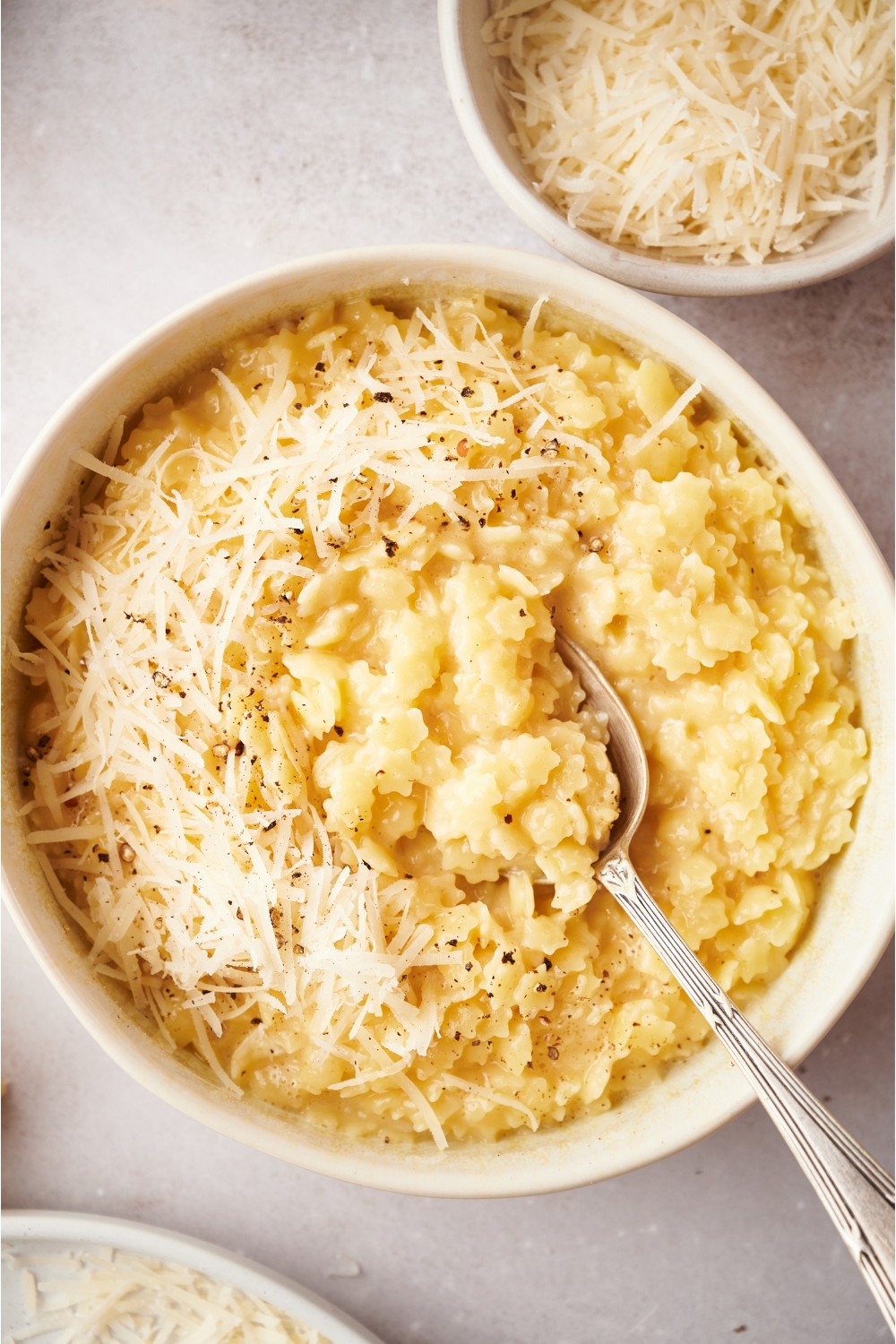 A bowl of pastina topped with parmesan cheese and pepper. A spoon is in the bowl.