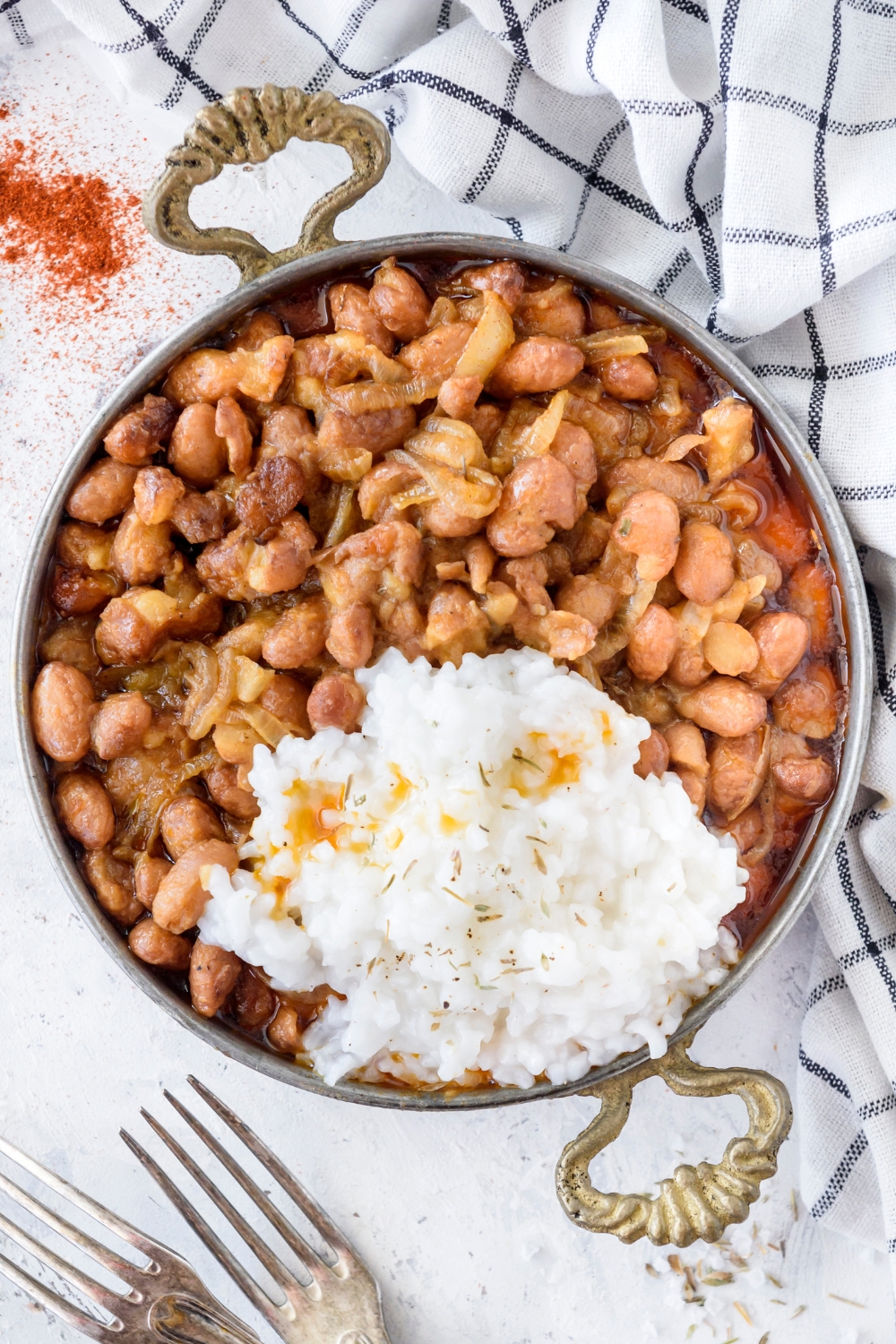 A bowl of cooked pinto beans mixed with cooked onions and a side of white rice.