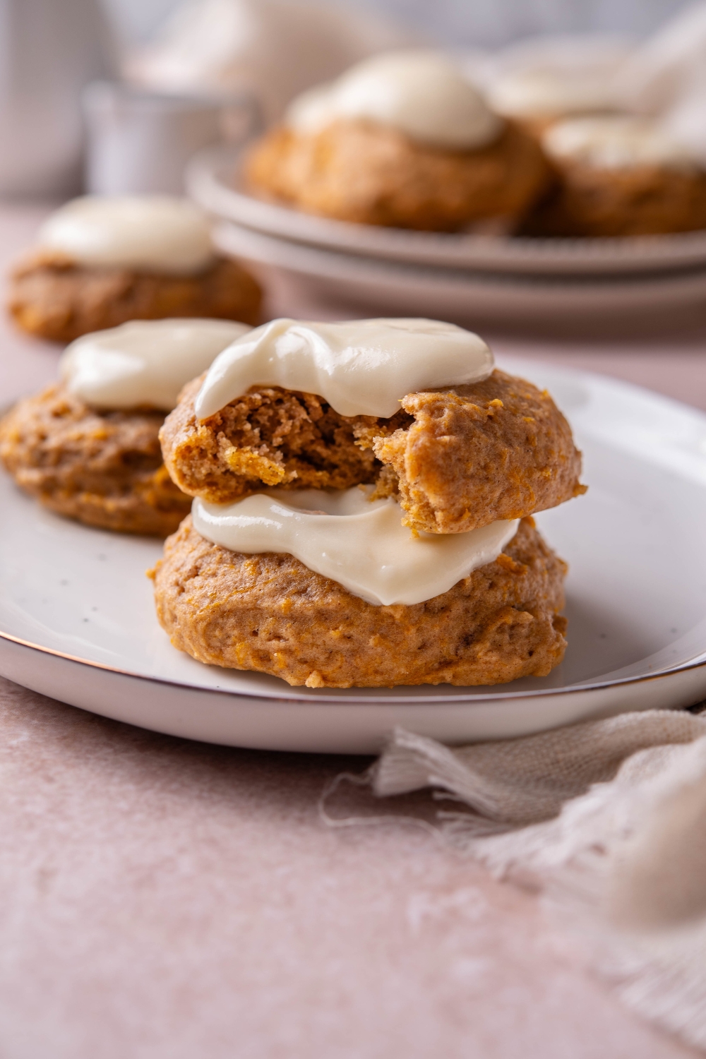 Two pumpkin cookies stacked on top of each other. Each is topped with frosting and the cookie on top has a bite taken out.