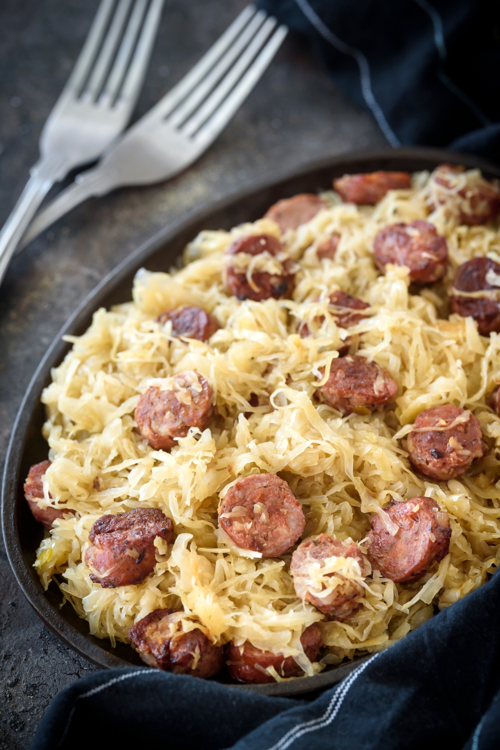 A plate filled with sauerkraut and sliced sausages. Two forks are next to the plate.