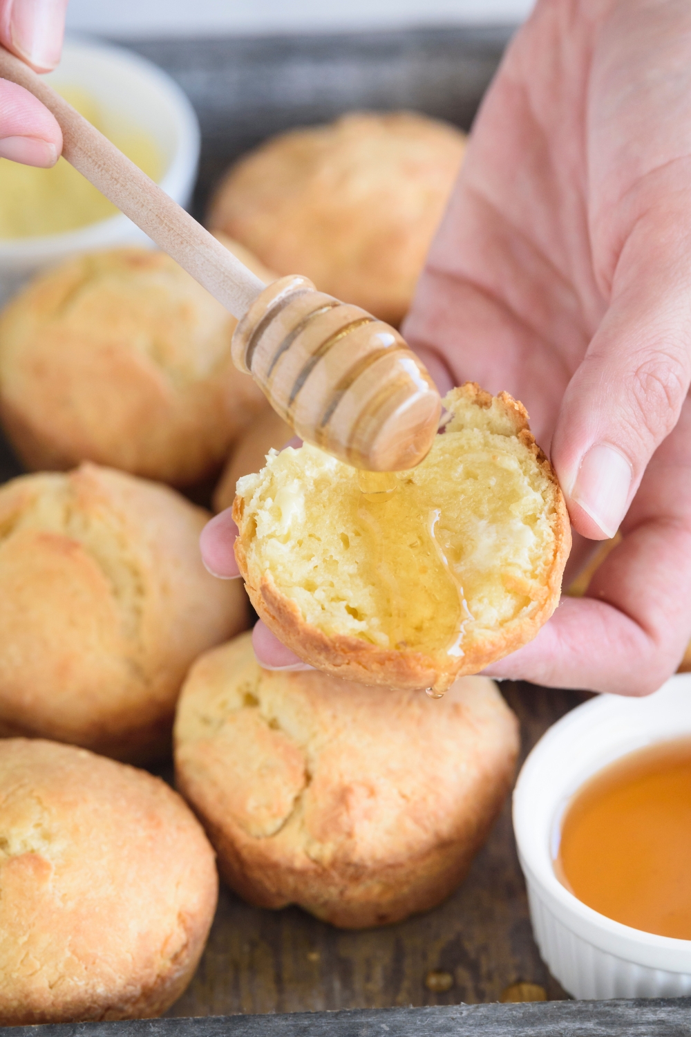 Hands drizzling baked biscuits with honey
