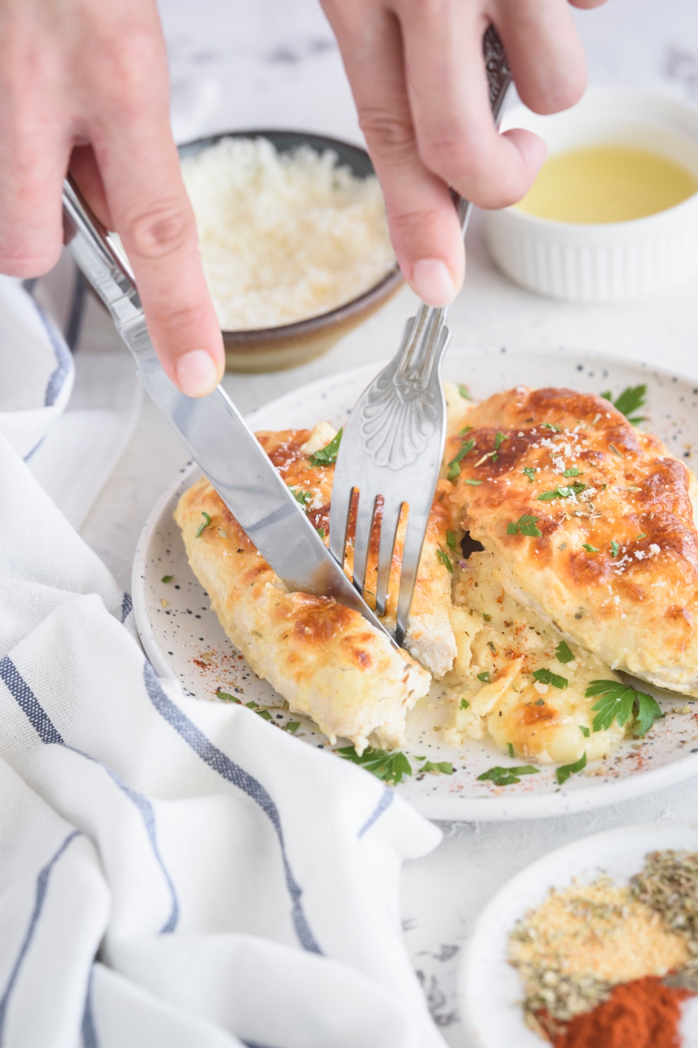 A person using a fork and knife to slice a piece of baked chicken breast.