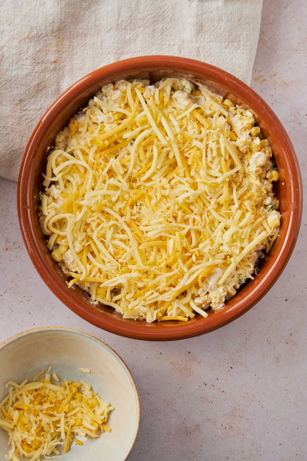 Shredded cheese on top of a jalapeno corn casserole in a red dish