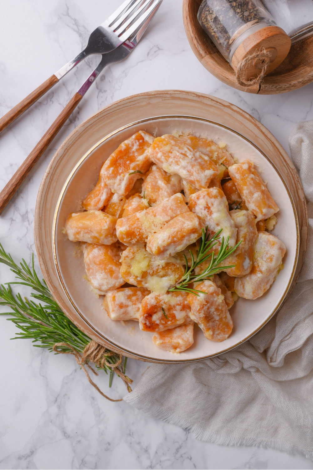 A bowl of sweet potato gnocchi covered in cream sauce with a sprig of rosemary garnished on top.