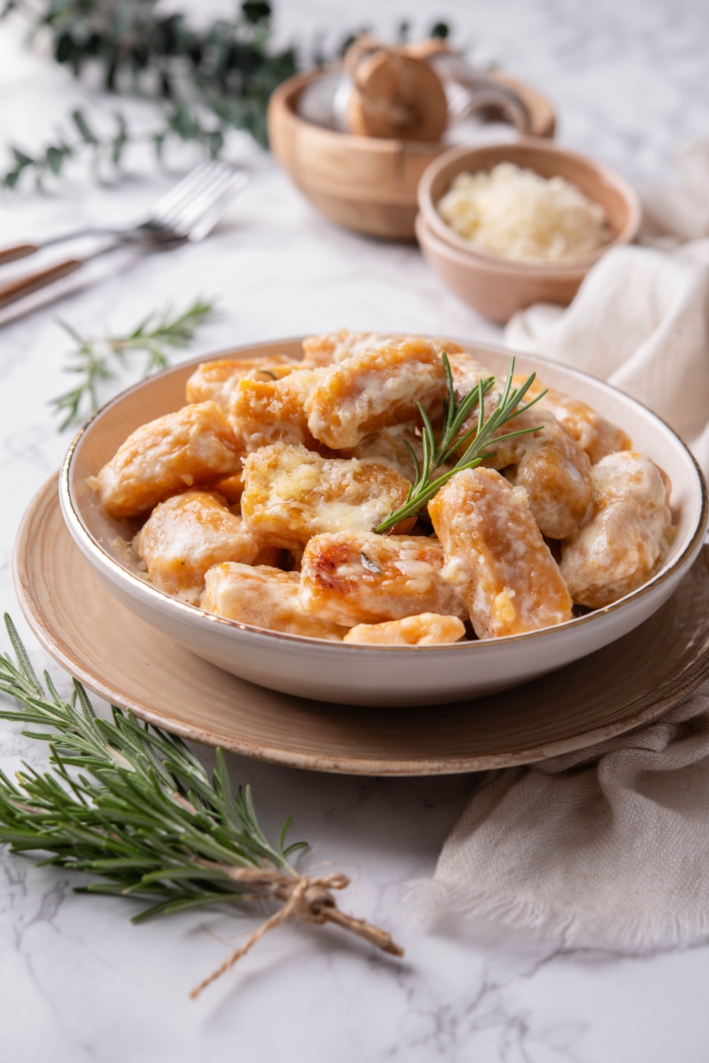 A bowl of sweet potato gnocchi covered in cream sauce with a sprig of rosemary garnished on top.