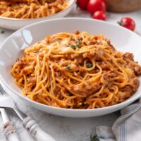 A bowl of spaghetti in a red creamy sauce with melted cheese and ground beef.