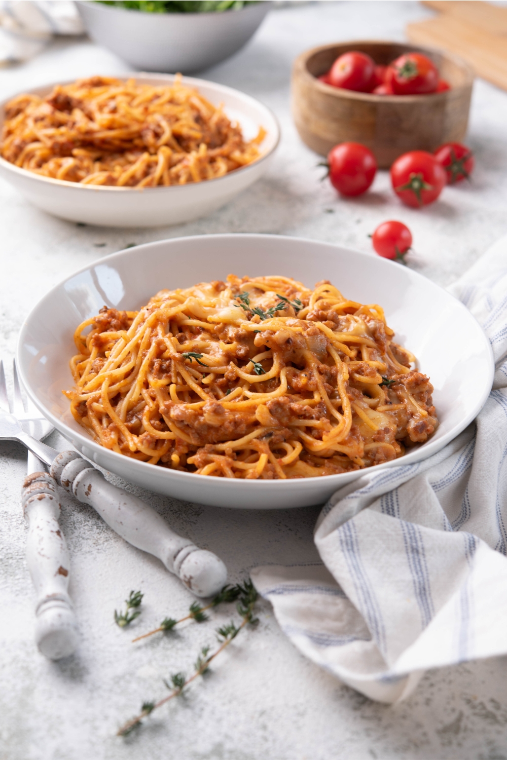 A bowl of spaghetti in a red creamy sauce with melted cheese and ground beef. A second bowl of spaghetti is in the background.