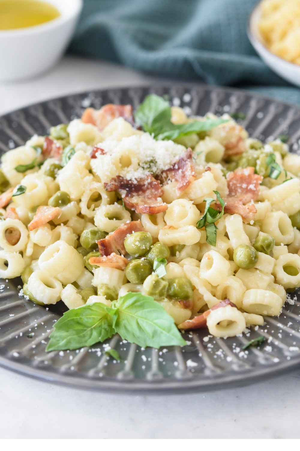 cooked pasta with peas and bacon served on a black plate with basil leaves garnish