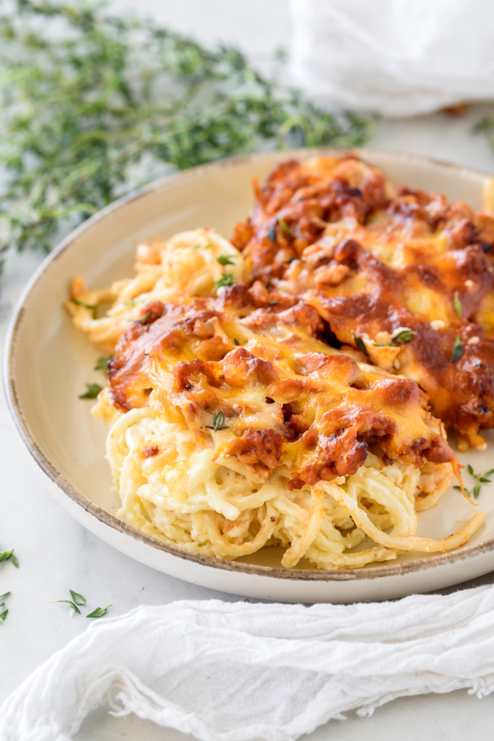 A bowl of baked spaghetti in white sauce covered in melted cheese with chunks of sausage.