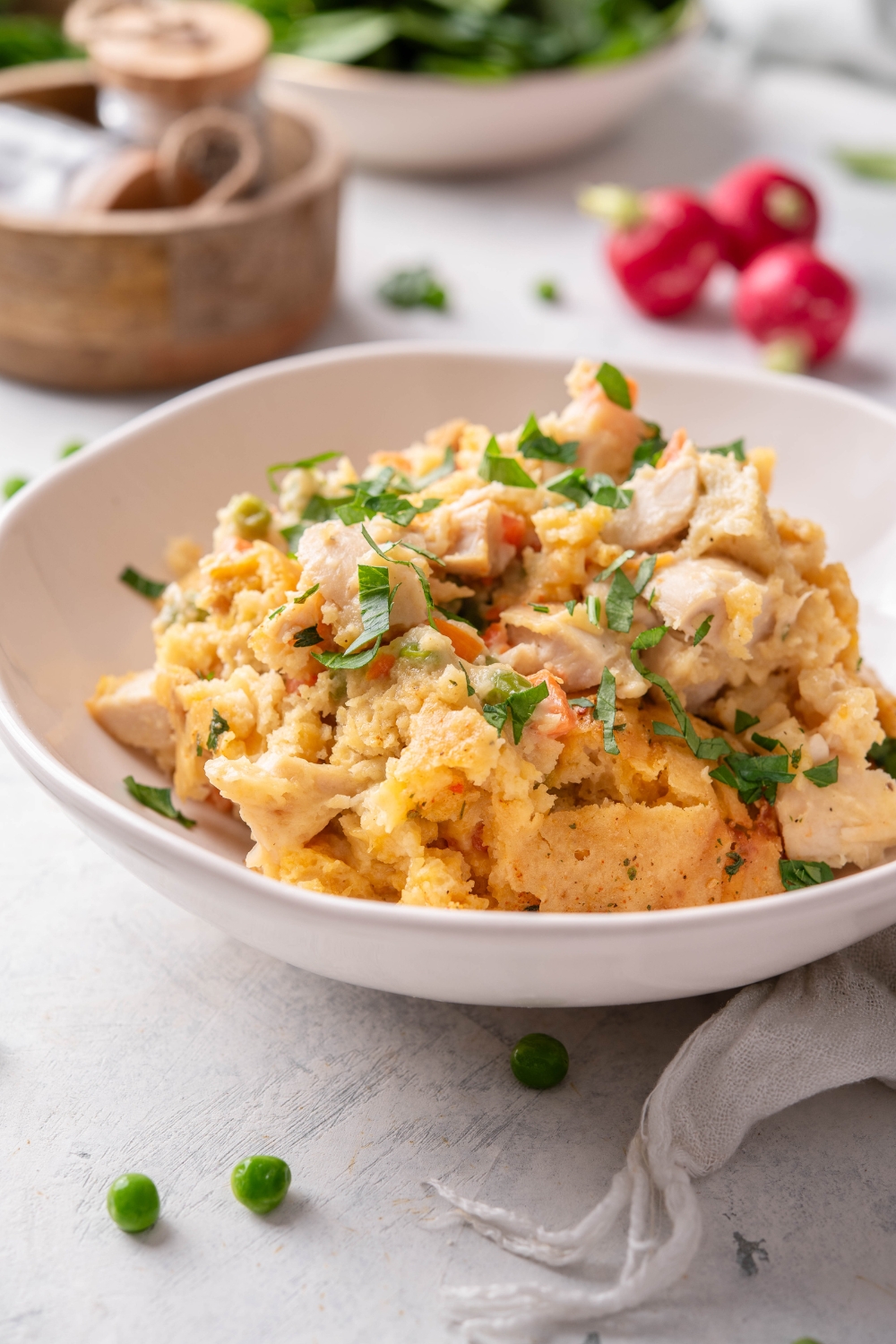 A bowl of chicken casserole with cooked chicken in a creamy sauce mixed with carrots, peas, and a crumbly biscuit topping and garnished with fresh herbs.