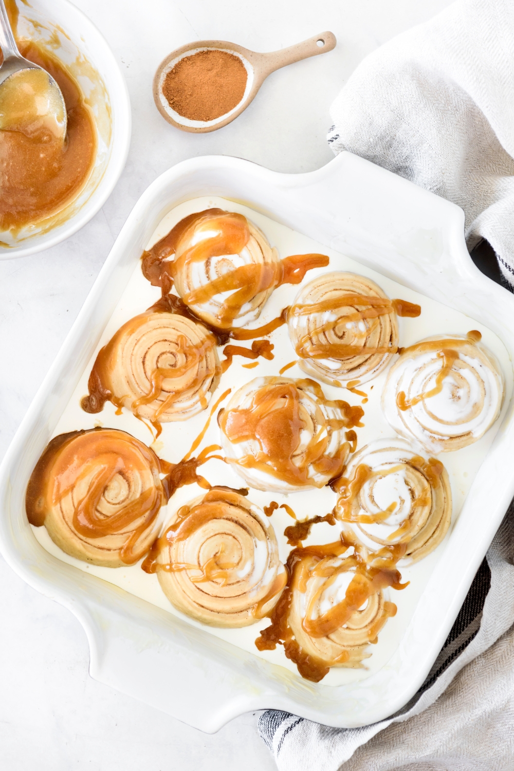 A baking dish filled with nine evenly-space cinnamon rolls covered in cream and drizzled with a brown sugar glaze.