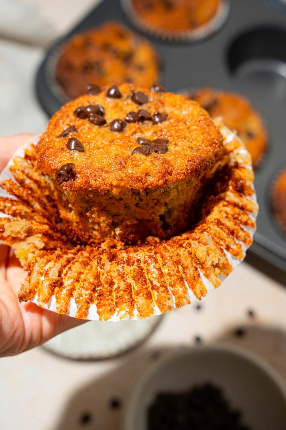 A hand holding a chocolate chip almond flour, banana muffin that is unwrapped.
