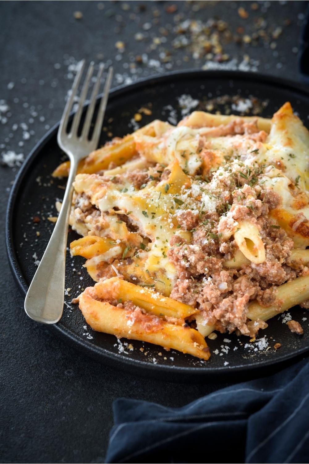 A plate with lasagna casserole topped with parmesan cheese and a fork sitting next to it.