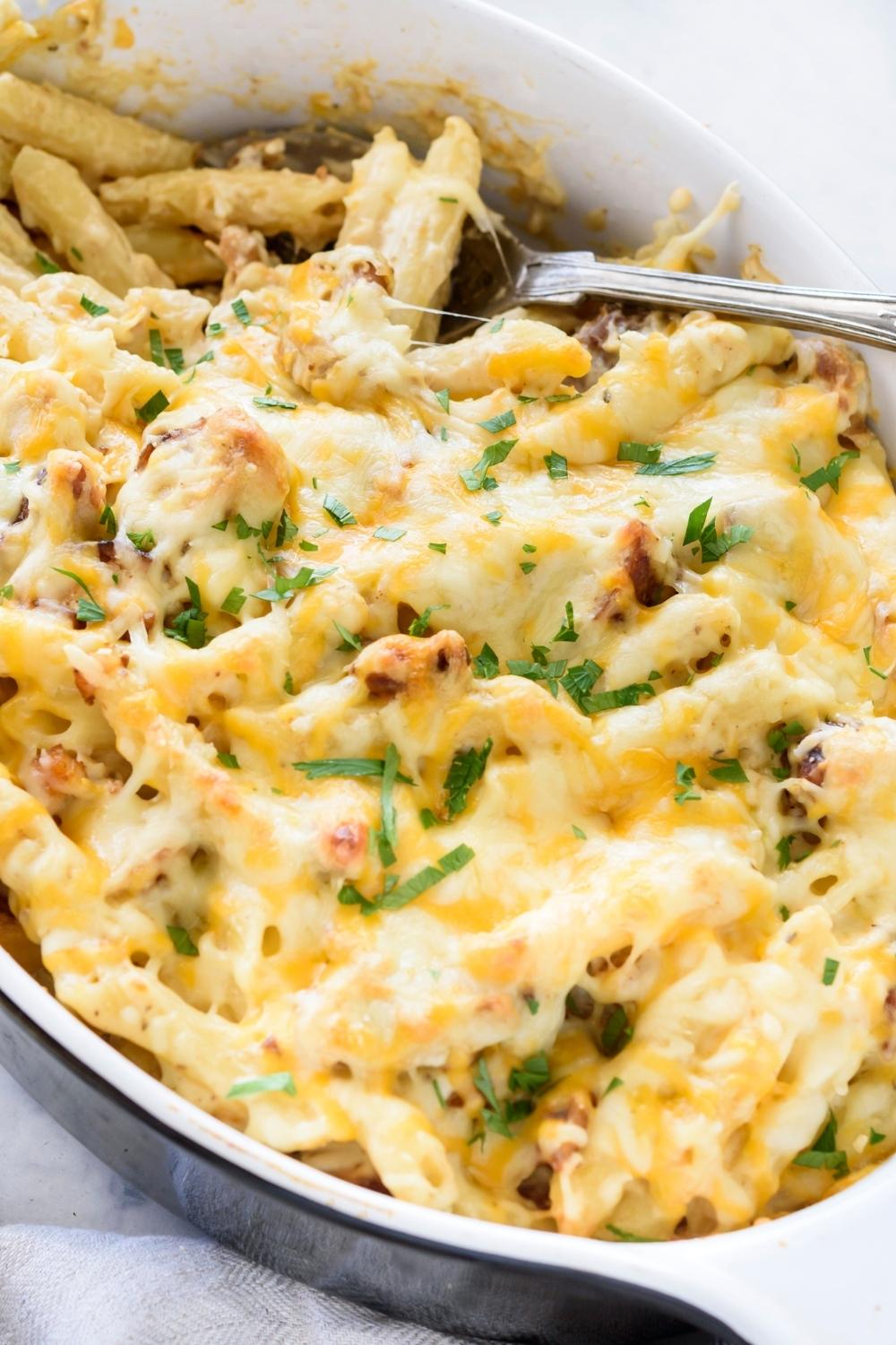 A casserole dish with chicken alfredo bake garnished with parsley.