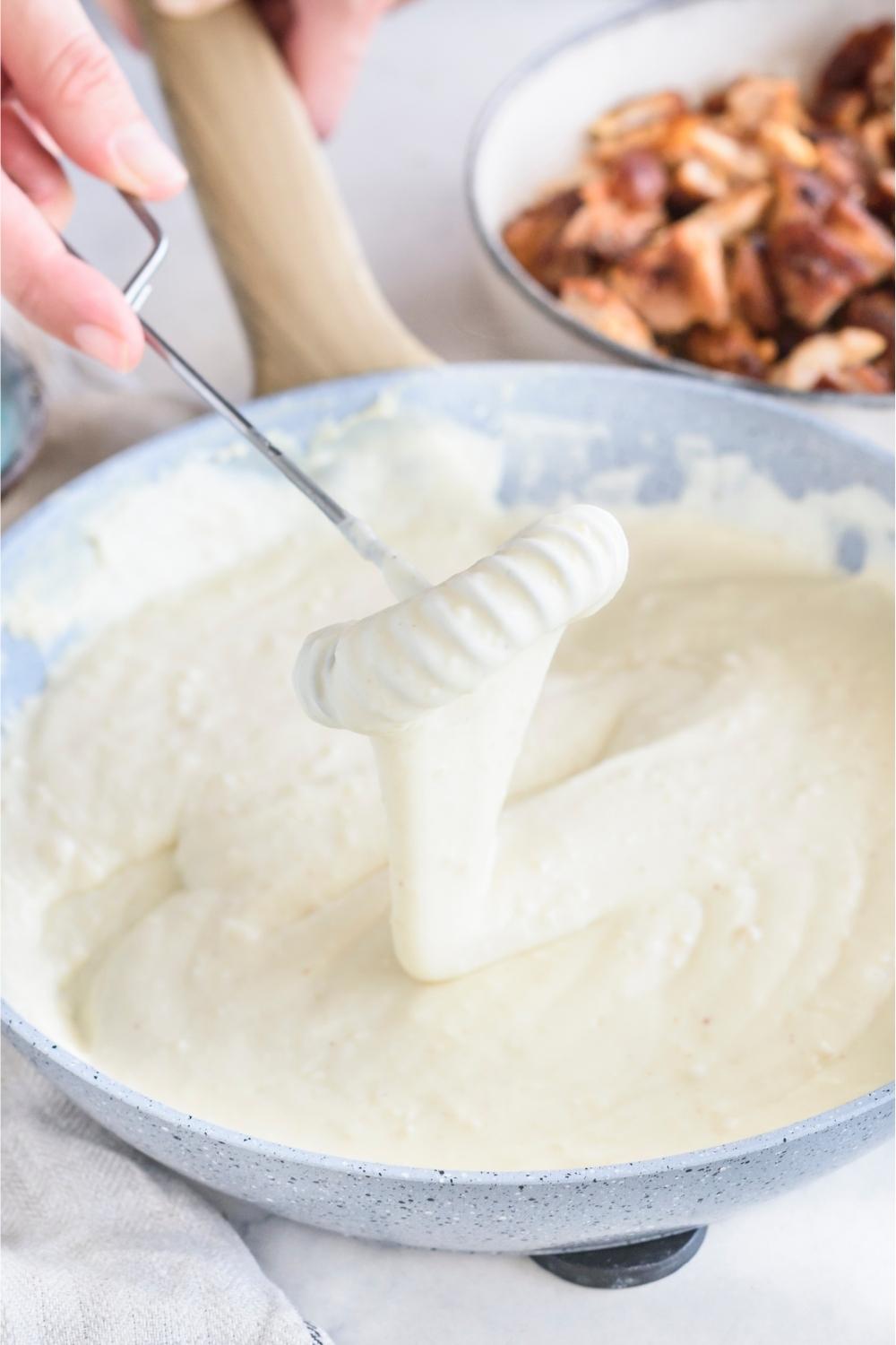 A skillet with creamy alfredo sauce being mixed.