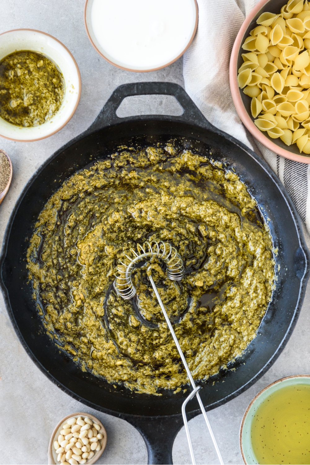 A skillet with basil pesto being mixed with oil.