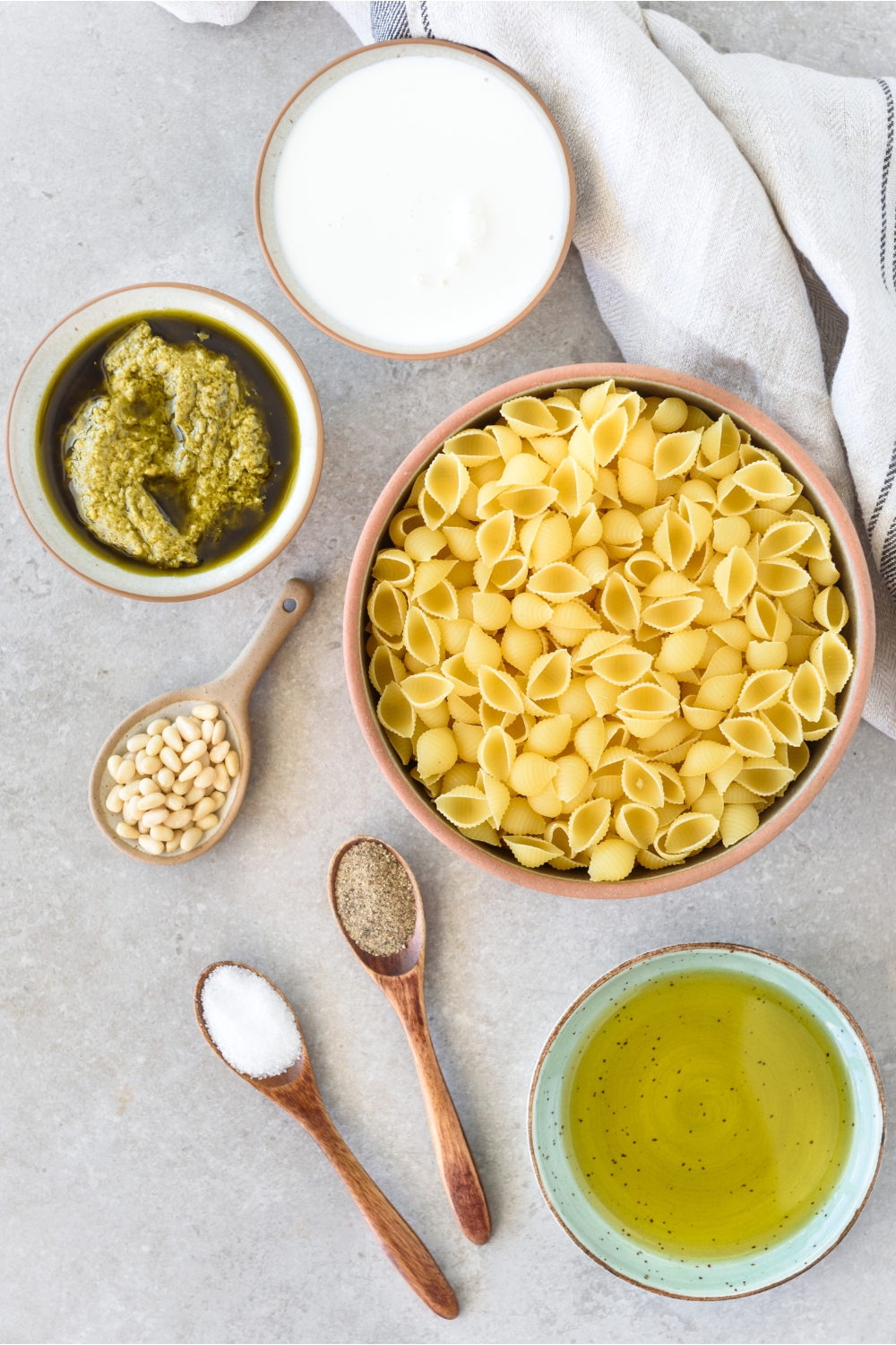 A countertop with pasta shells, pesto, pine nuts, heavy cream, oil, and salt and pepper.