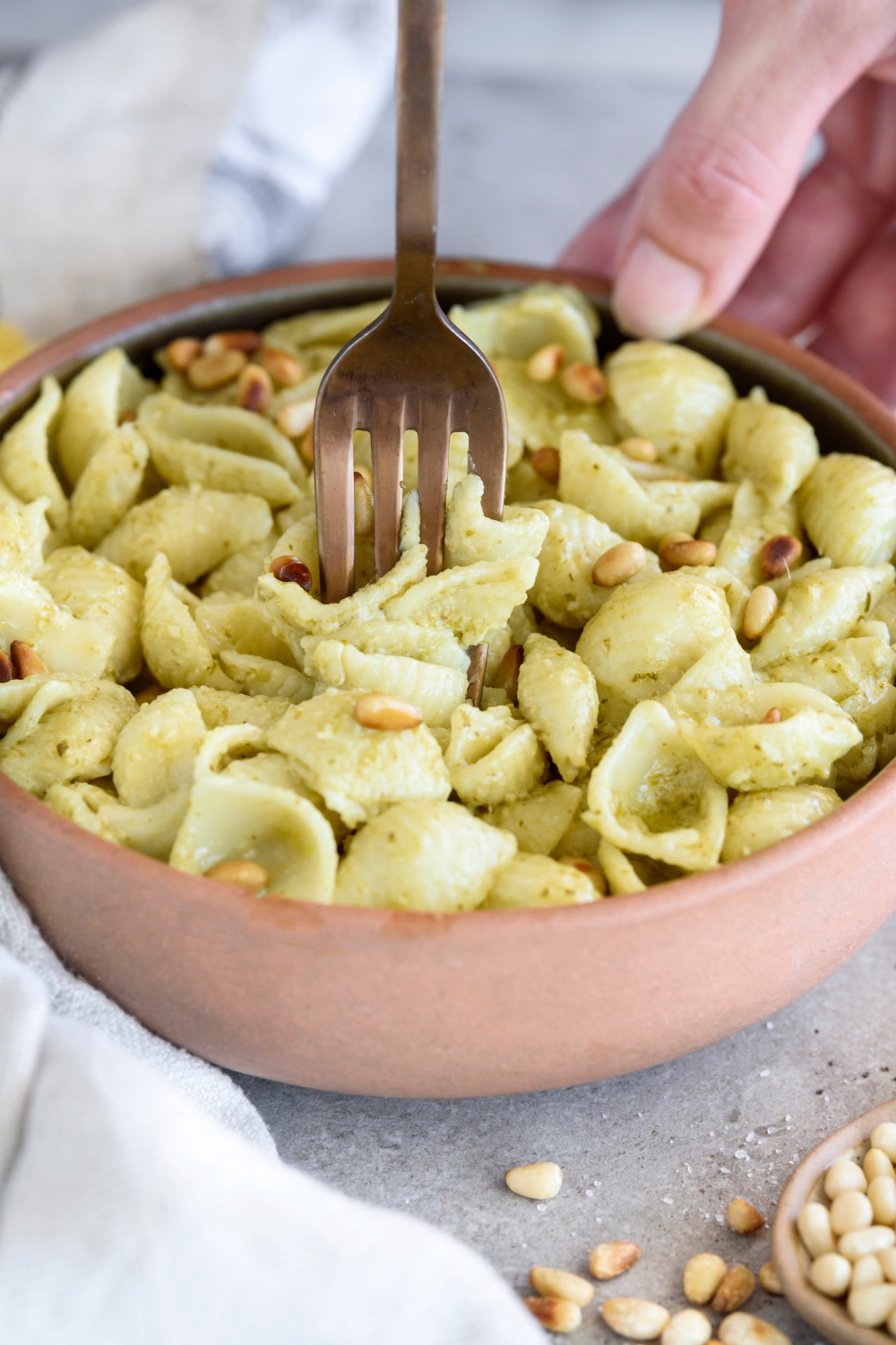 A bowl with creamy pest pasta topped with pine nuts. A fork is in the bowl.