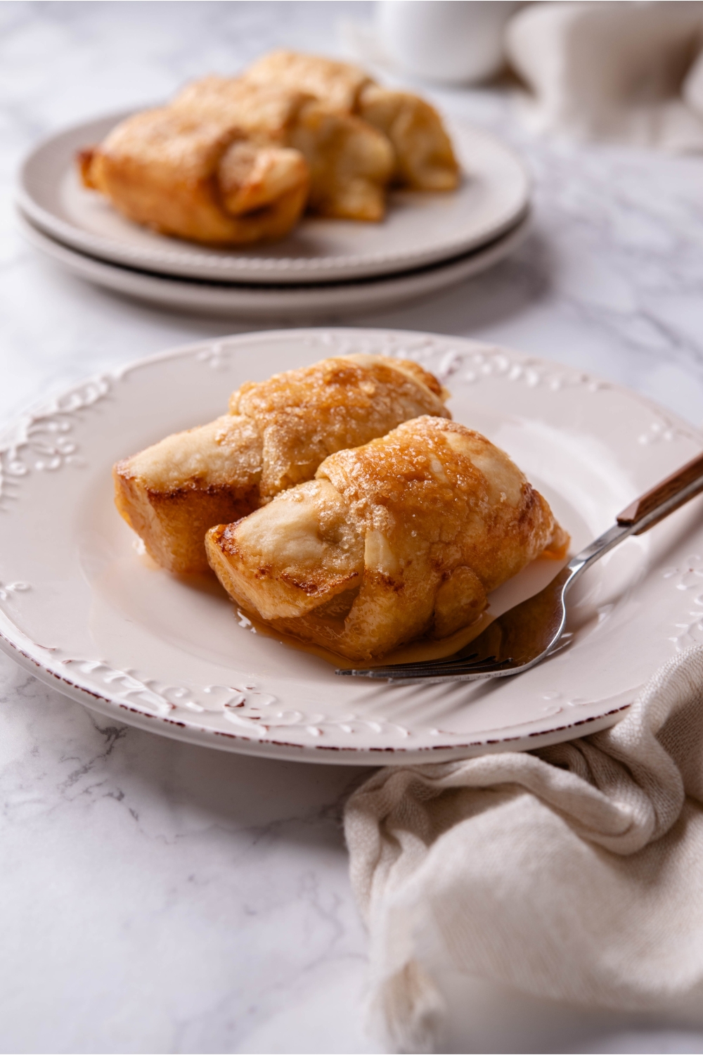 A plate with apple dumplings with crescent rolls and a fork next to them.