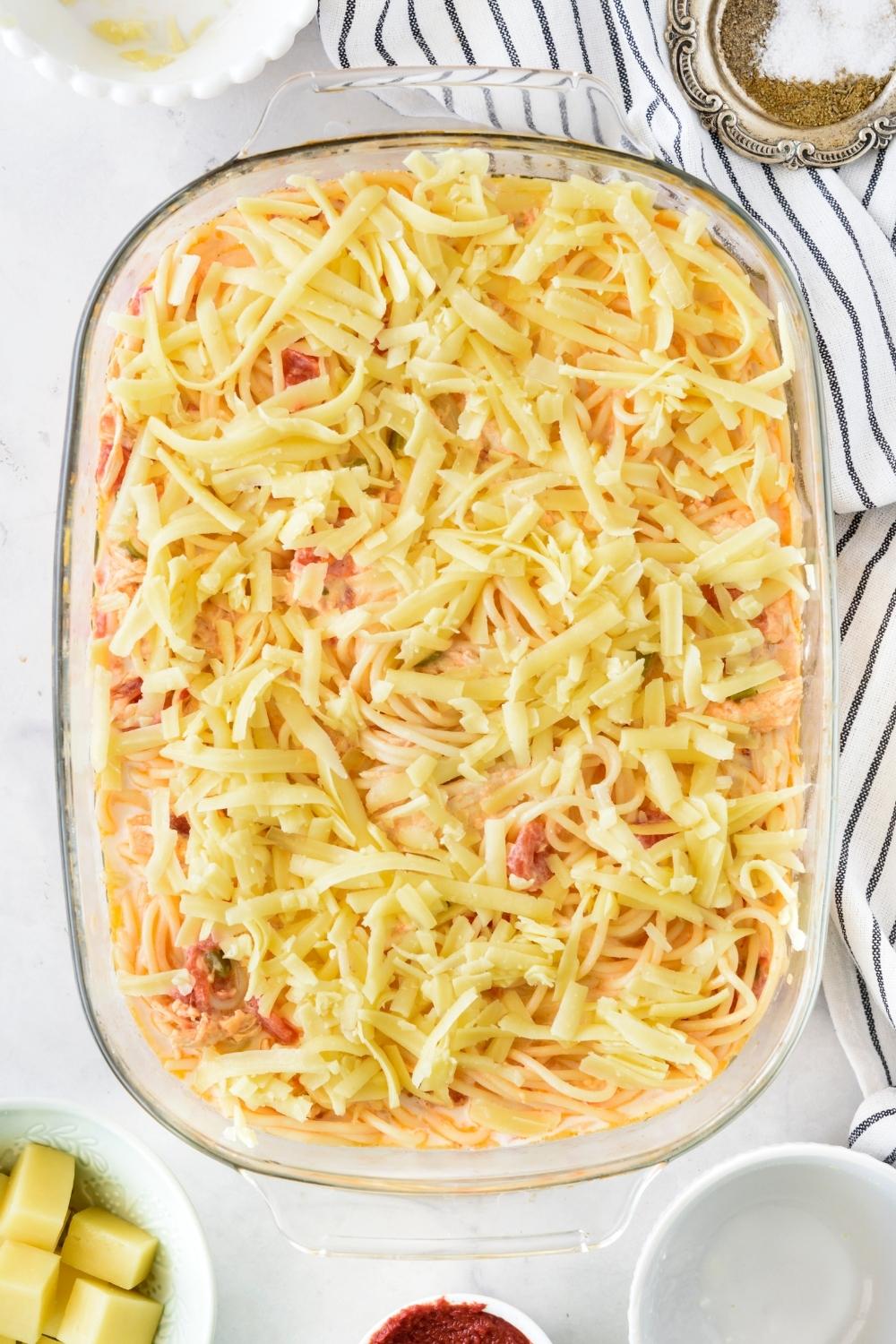 A casserole dish with unbaked casserole topped with shredded cheese.