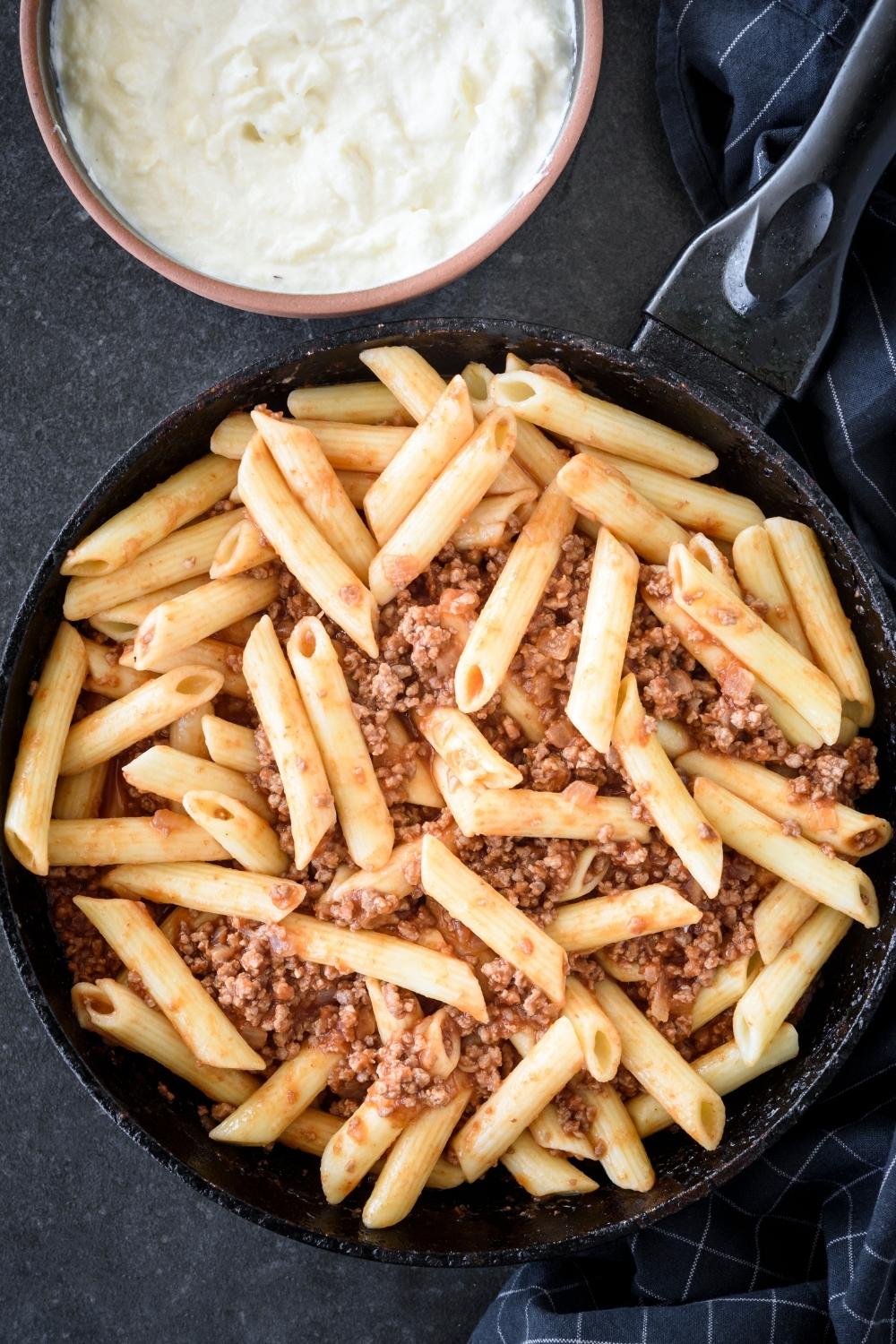 A skillet with the beef mixture and pasta being combined.