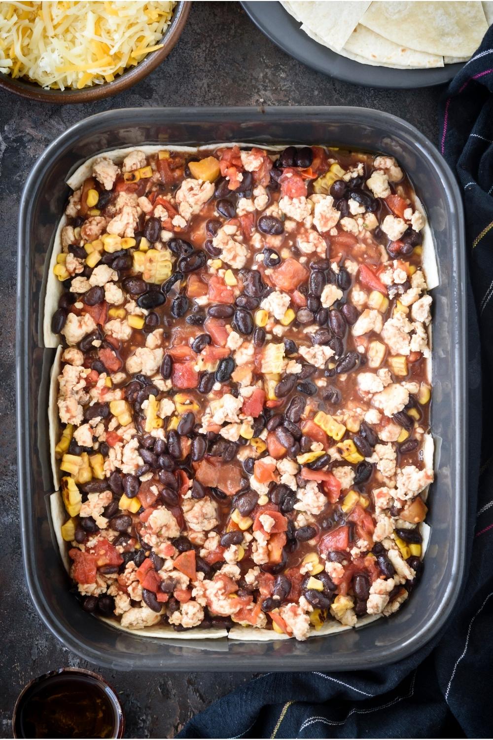 A casserole dish with the layer of tortillas covered with the bean mixture.