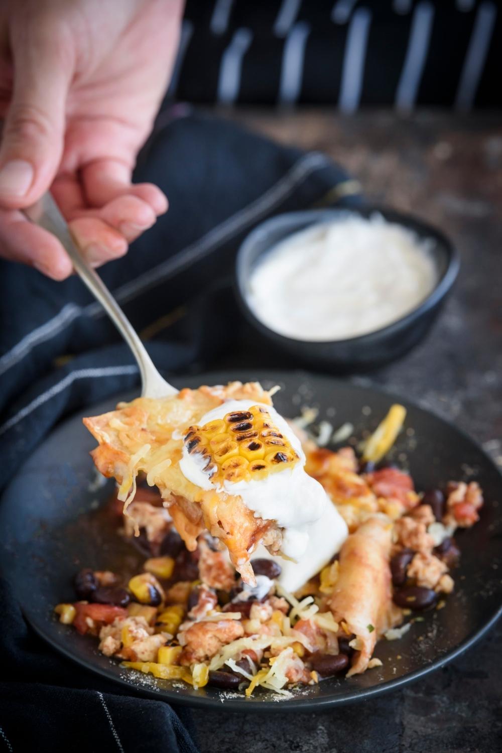 A fork holding up a large scoop of ground chicken casserole over a plate with a serving of ground chicken casserole topped with sour cream.