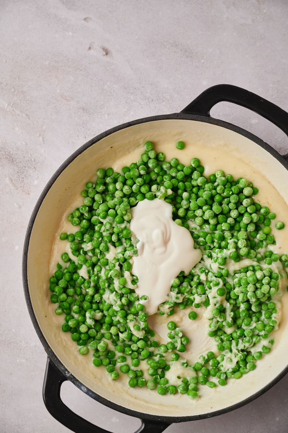 A skillet with the peas and heavy cream being added to the white sauce.