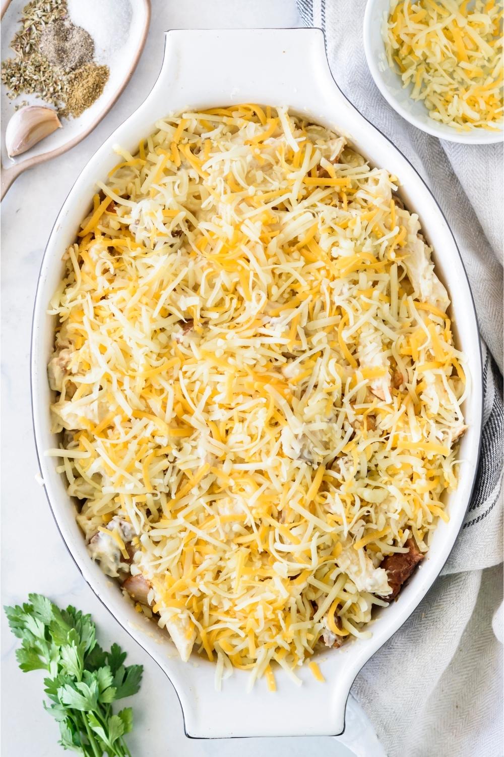 A casserole dish with unbaked chicken alfredo casserole topped with shredded cheese.