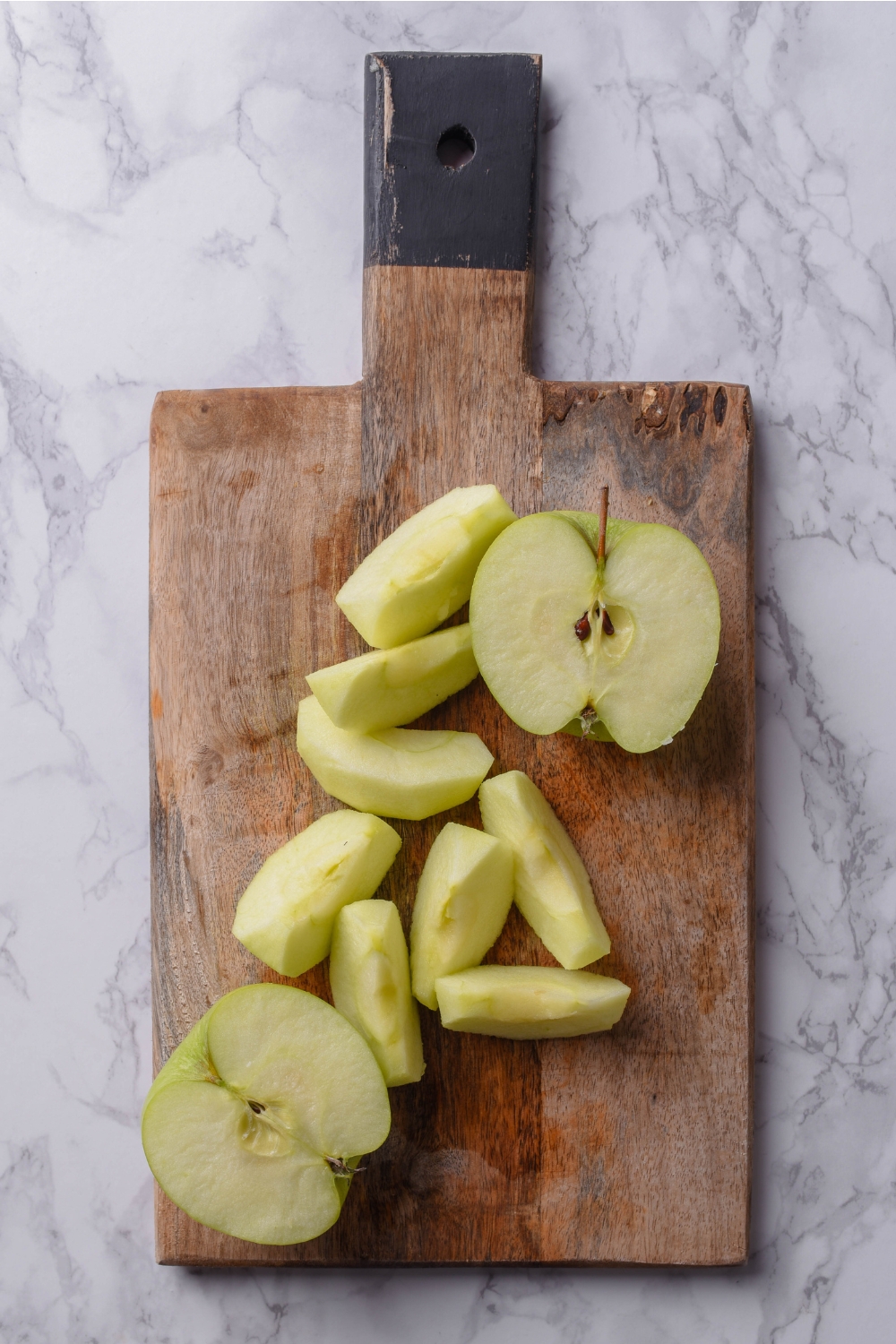 A cuttingbpard with granny smith apples being sliced.