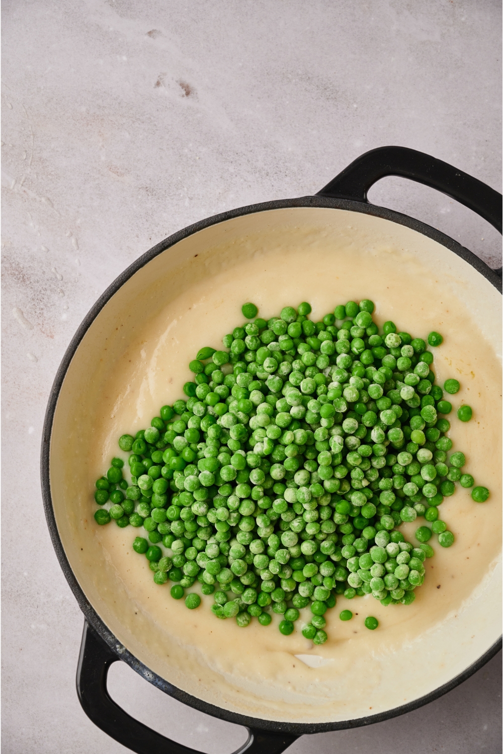 A skillet with the peas being added to the white sauce.