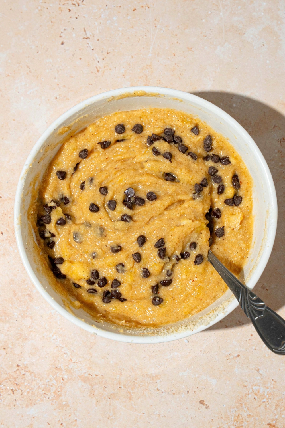 A smooth almond flour, banana muffin batter with chocolate chips mixed throughout in a white bowl.
