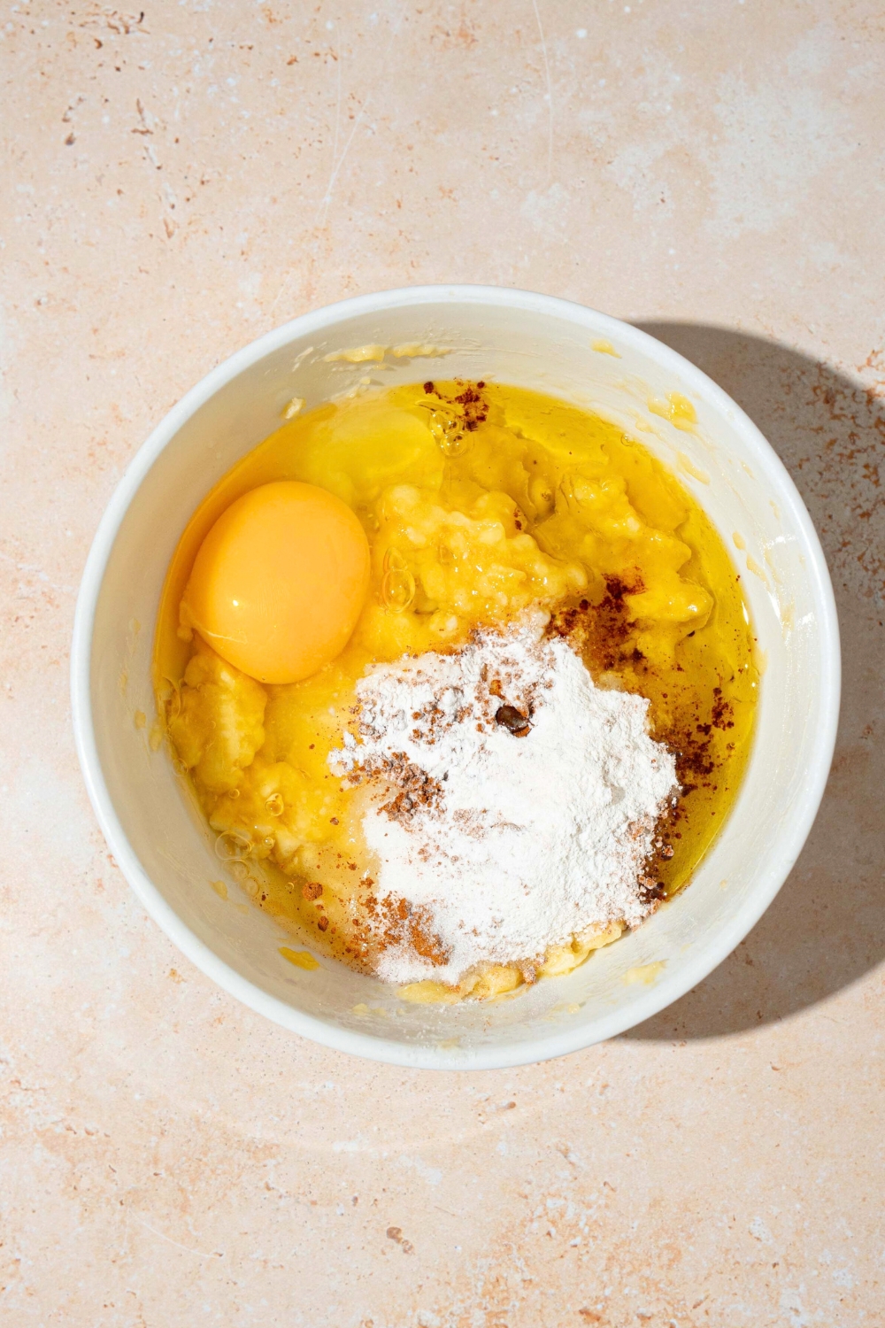 Baking powder, cinnamon, mashed banana, and an egg in a white bowl.