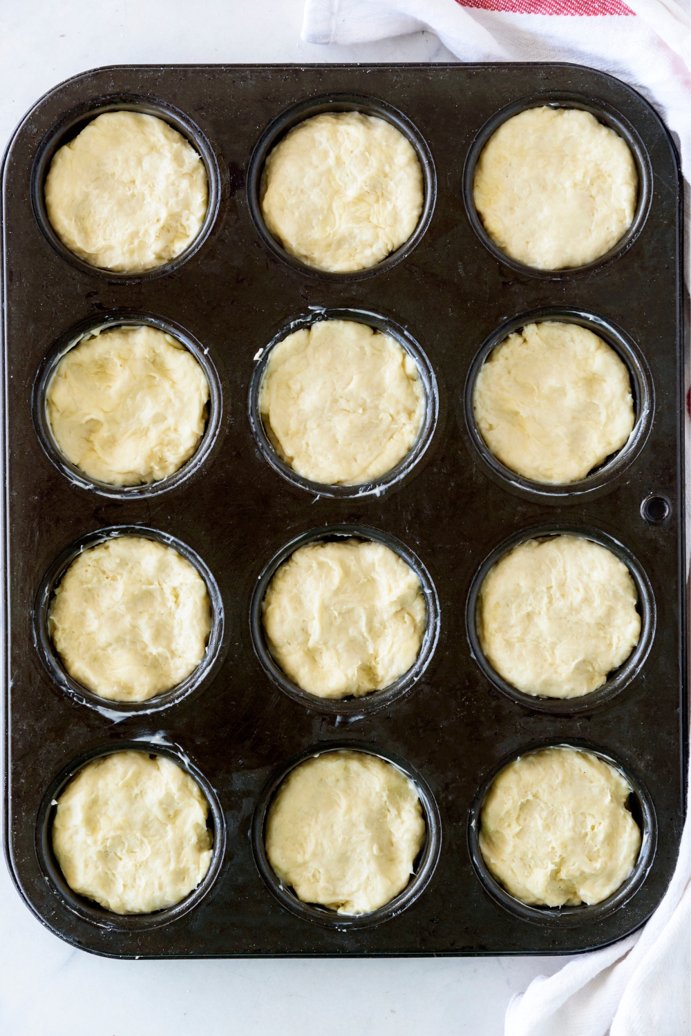 Raw biscuit dough in a black muffin pan