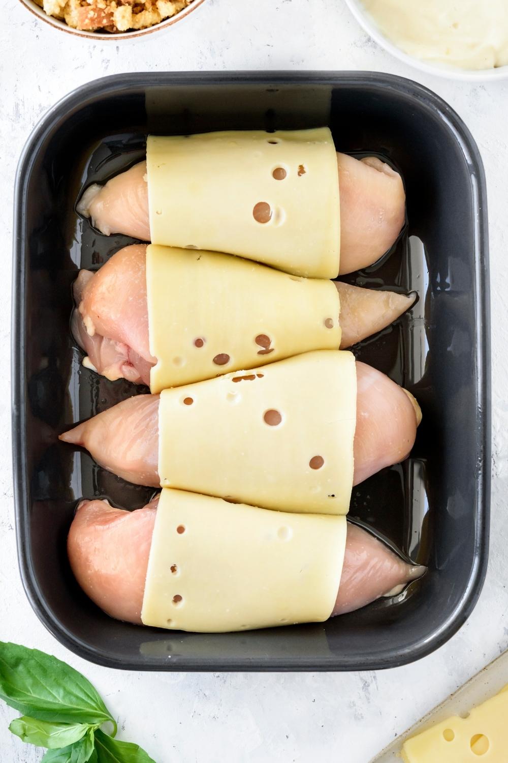 A casserole dish with chicken breast covered with a slice of swiss cheese.