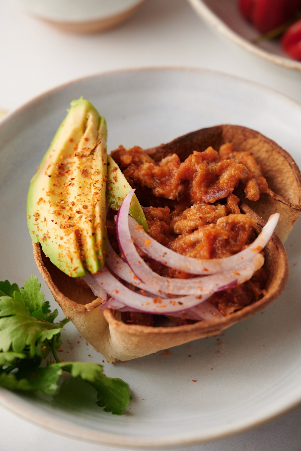 Cooked mexican chili in a tortilla bowl with onion and avocado on a white plate