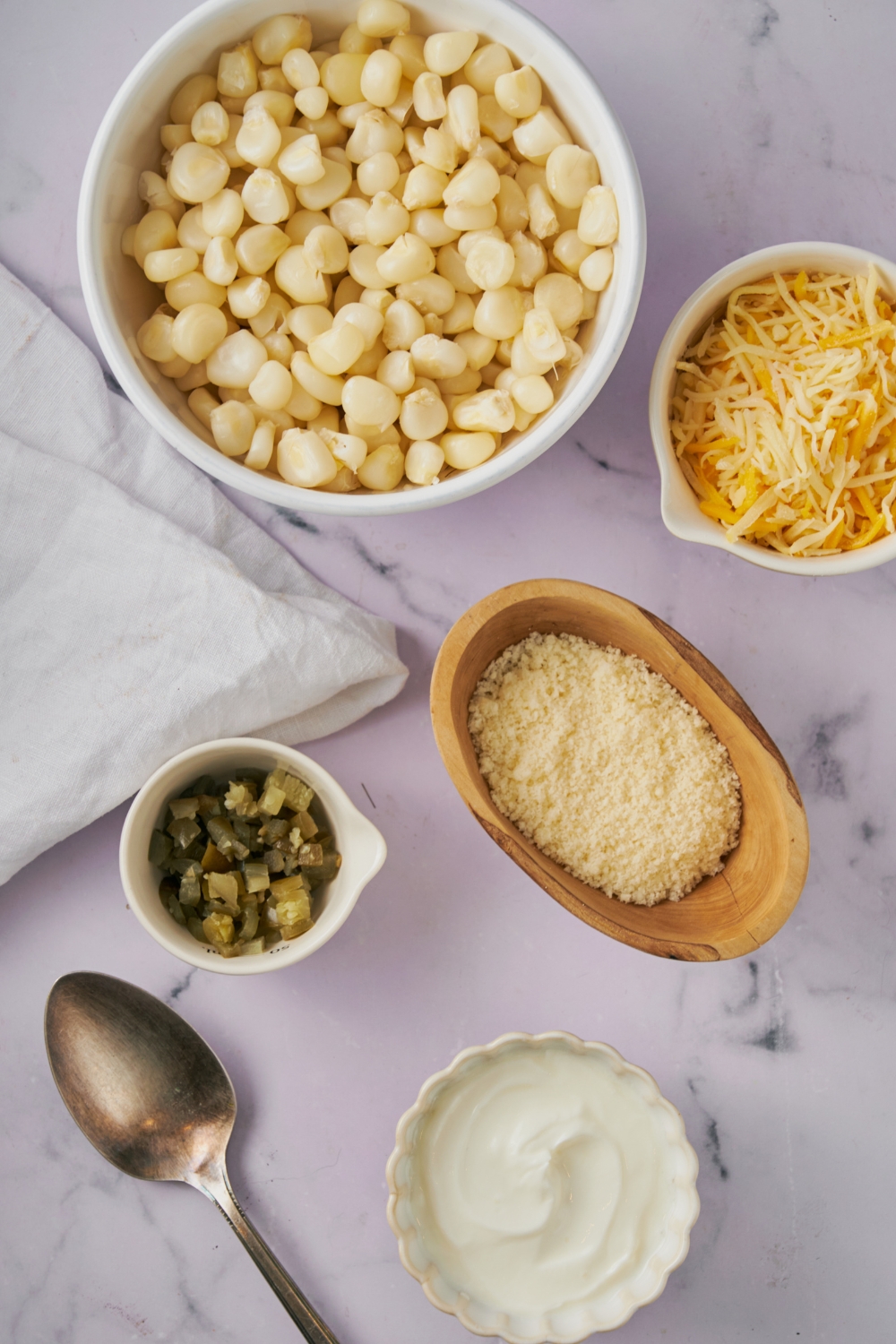Hominy, jalapenos, shredded cheeses in separate bowls on a marble countertop