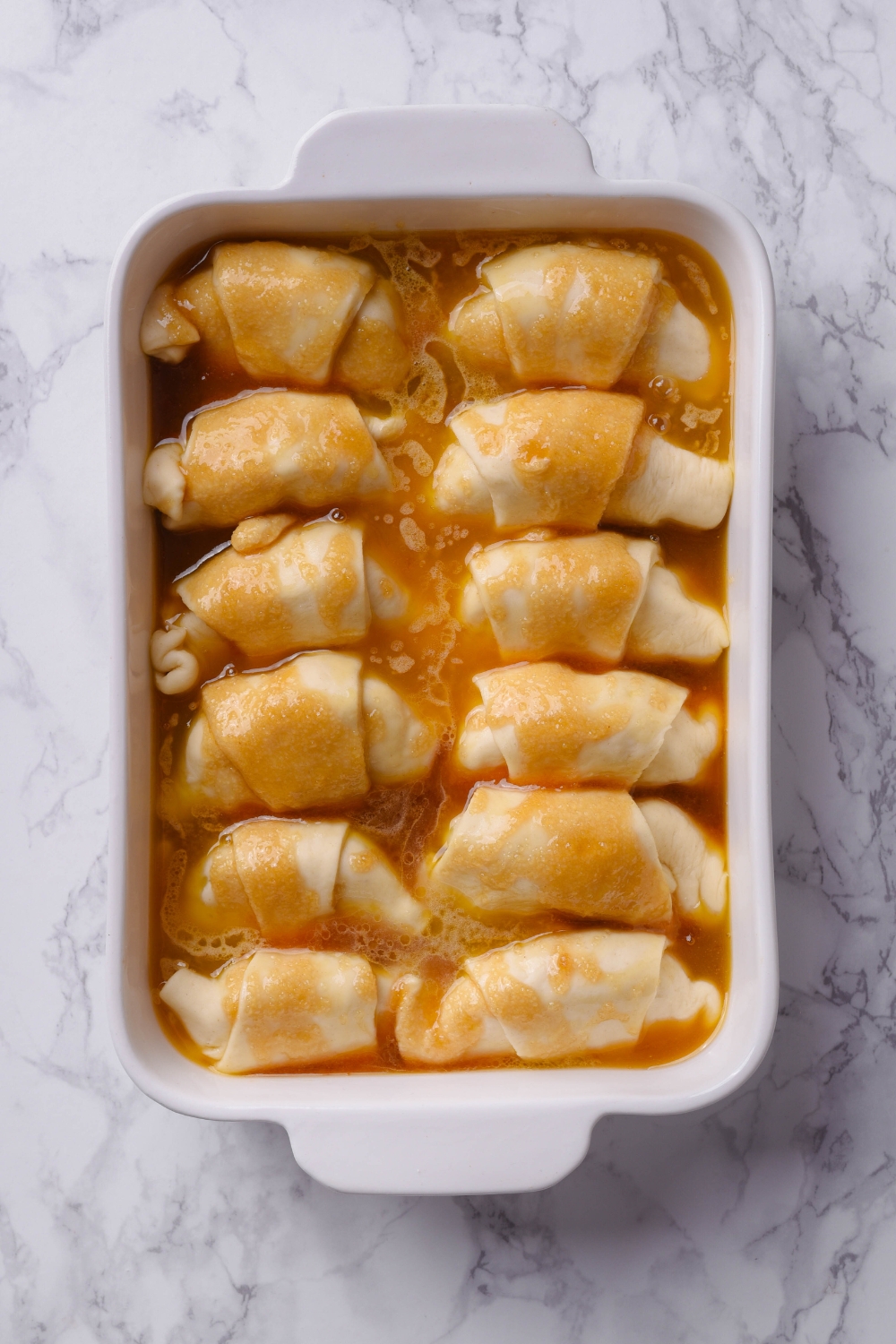 A casserole dish with unbaked crescent rolls with soda between them.