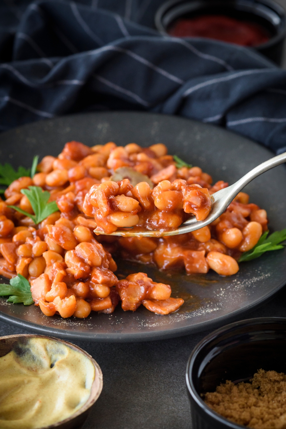 A fork with baked beans on it over a plate with more baked beans.