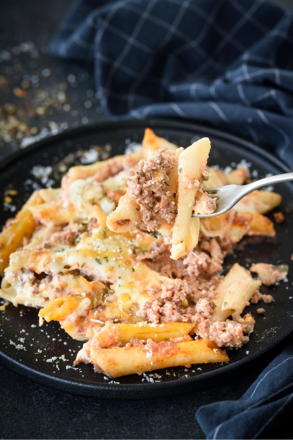 A plate with lasagna casserole topped with parmesan cheese. A fork has a heaping scoop of lasagna casserole.