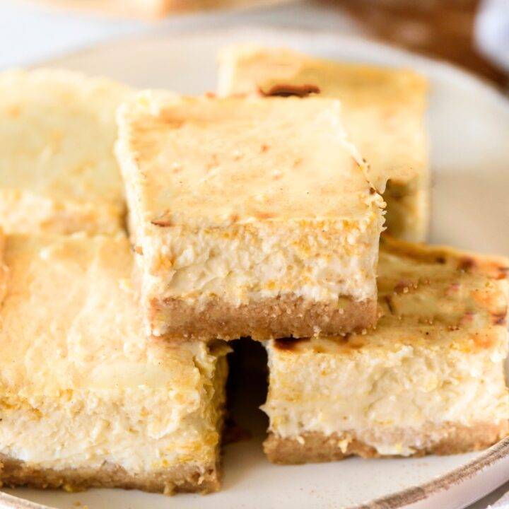 A bunch of pumpkin cheesecake bars stacked on a white plate.