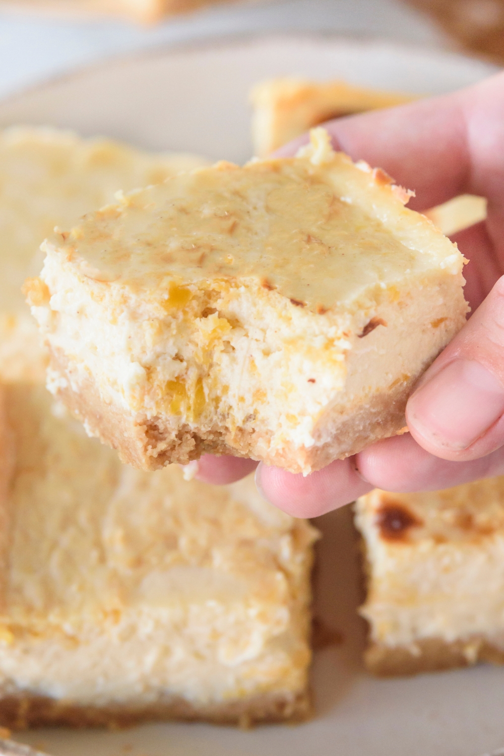 A pumpkin cheesecake bar being held above a plateful of bars.