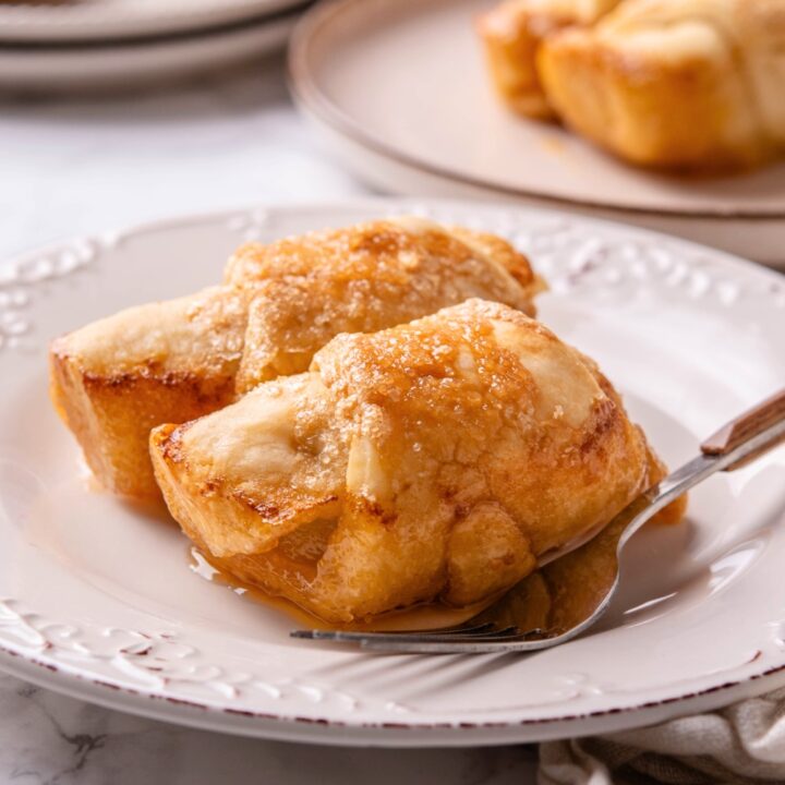 Two crescent roll apple dumplings on a white plate with a fork.