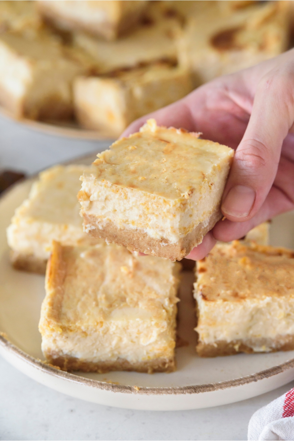 A pumpkin cheesecake bar being held above a plateful of bars.