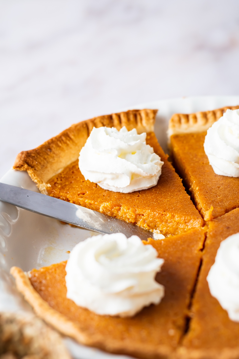 Two slices of sweet potato pie in a white dish with a knife in it.